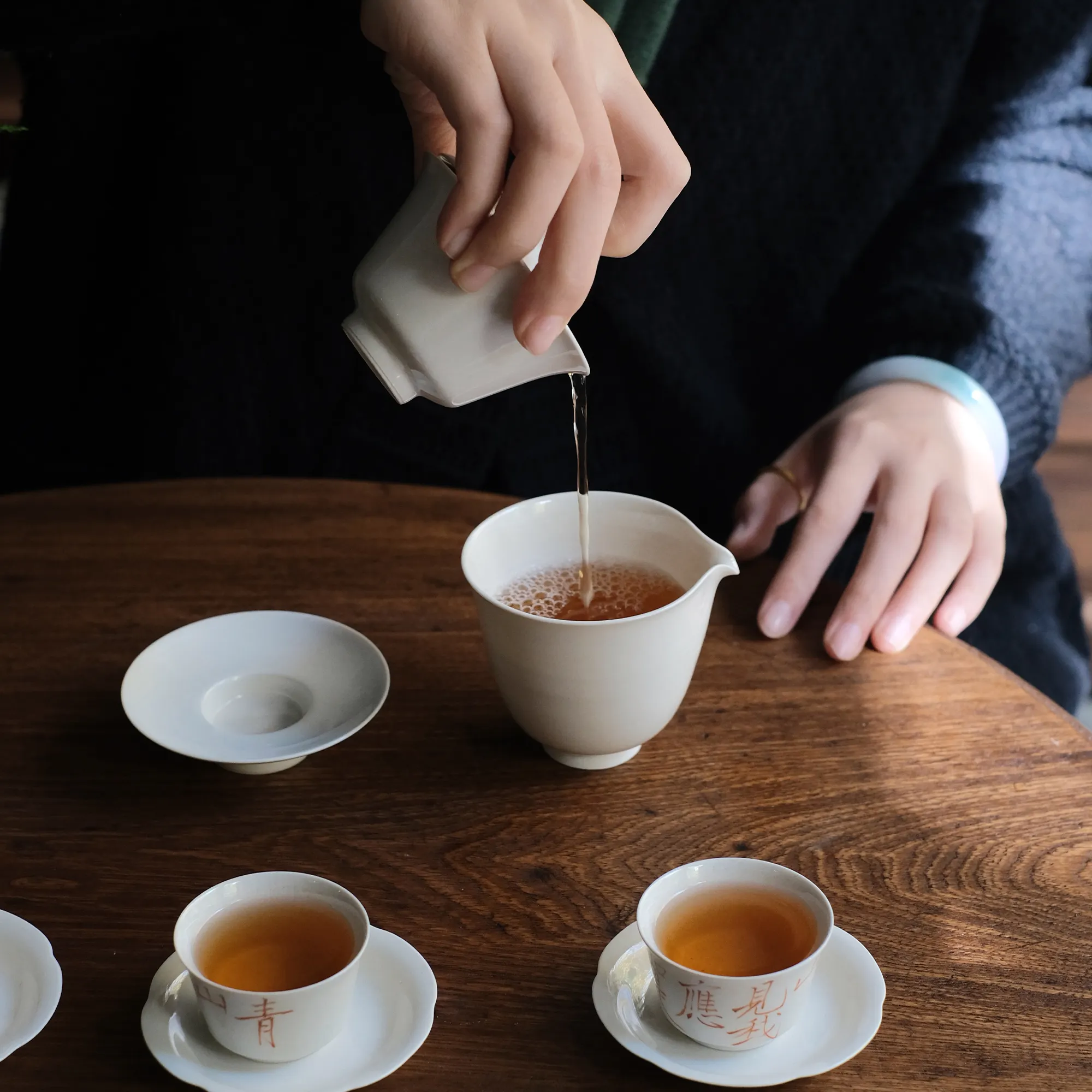 Pouring tea from a gaiwan into a fairness pitcher with fingers held near the rim